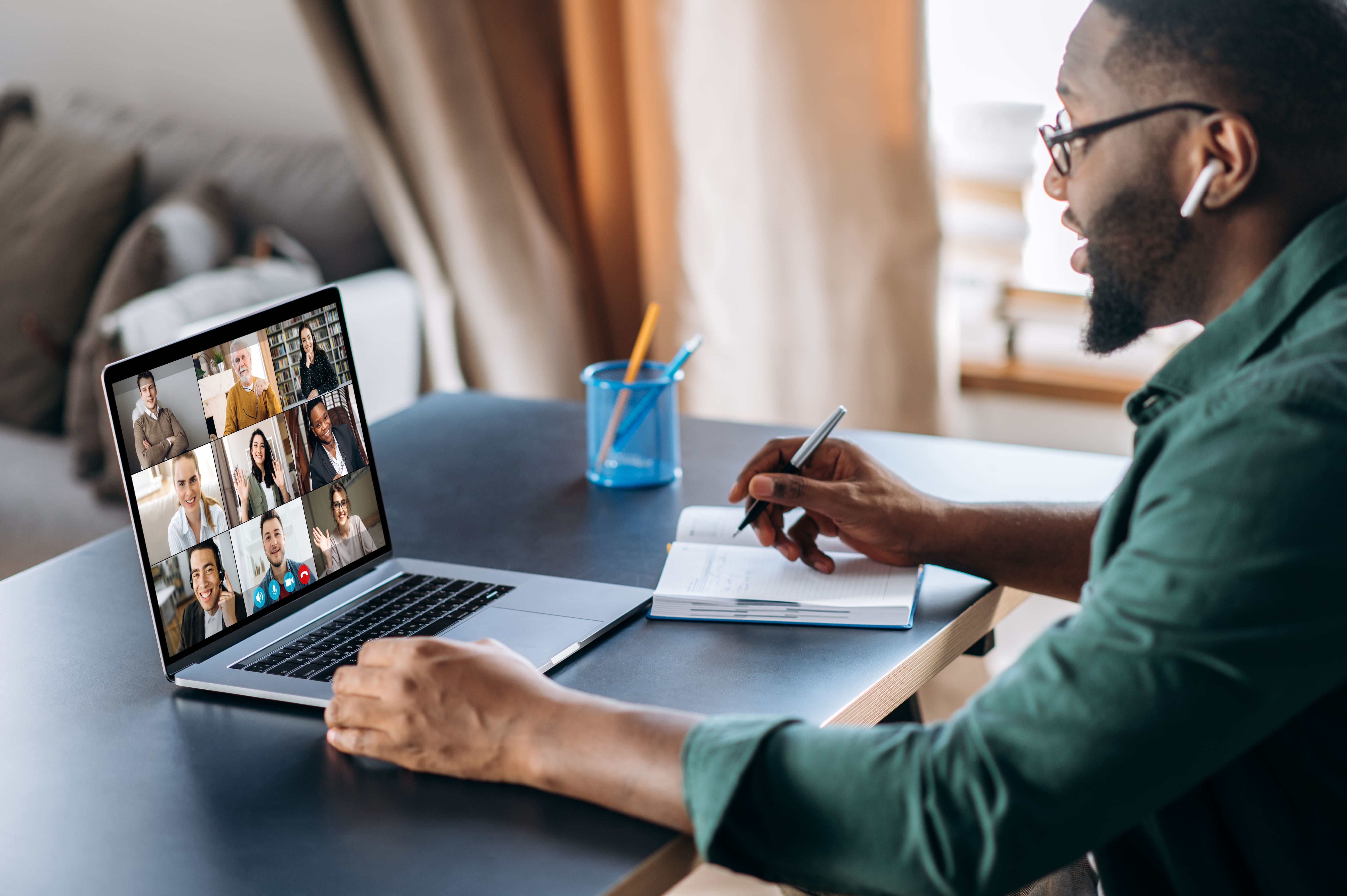 Man on laptop with notepad on Teams call smiling
